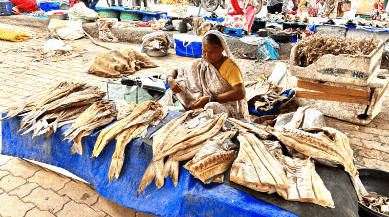 A woman sitting on the ground in a market behind a table full of fish.