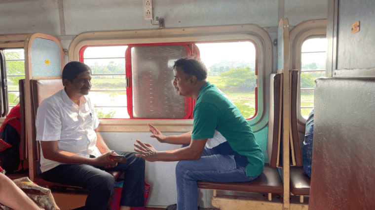Two people on a train are facing each other talking.
